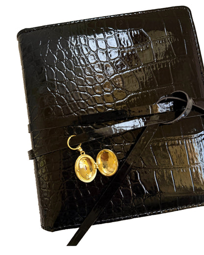 Open locket charm on the black croc embossed Elali journal on a clean white background